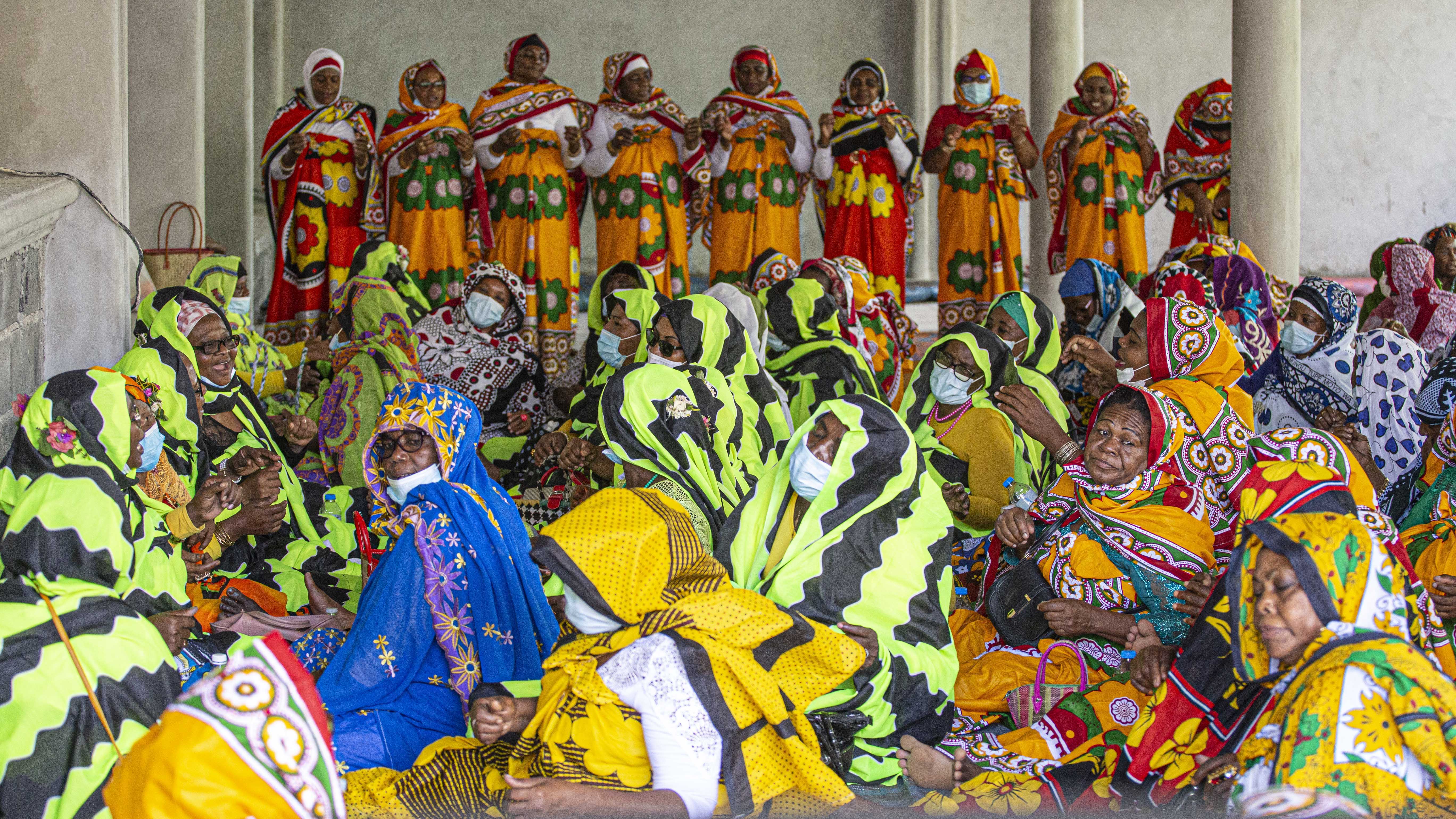 Cérémonie de mawlida shenge en journée sur une terrasse couverte d'une mosquée avec en arrière-plan des femmes qui dansent, 6 juin 2021 à Tsimkoura © Ibrahim M'COLO